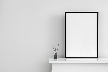Blank frame with reed diffuser on mantelpiece near light wall