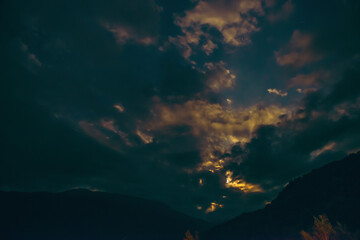 Naklejka premium The orange full moon rising from behind the mountain range illuminates the misty clouds, creating a mystical atmosphere. supermoon.the rising moon in the gorge of the Caucasus Mountains. long exposure