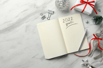 Inscription 2022 Goals written in planner and Christmas decor on white marble background, flat lay. New Year aims