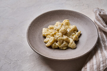 Close up homemade gnocchi, prepared with potato and whole grain flour dough with cream sauce on gray concrete background with napkin