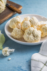 Raw cauliflower slices in a light bowl on a blue background with copy space.