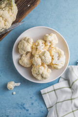 Raw cauliflower slices in a light bowl on a blue background with copy space.
