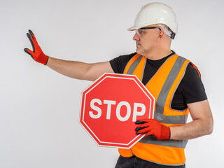 Restriction due to renovation work. Stop sign in hand of builder. Road worker in hard hat and orange vest. Concept of danger due to road work. Prohibiting sign STOP in hand of builder. Danger on road