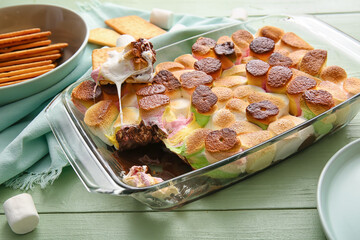 Baking dish with delicious S'mores dip and crackers on color wooden background, closeup