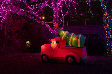 A Christmas inflatable decoration of Santa driving in a red truck with a christmas tree in the back.