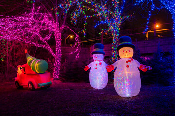 A pair of Christmas inflatable snowmen stand by as Santa drives a Christmas tree away in his truck.