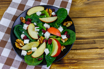 Autumn spinach salad with apple, feta cheese, walnut and dried cranberry on wooden table. Top view. Healthy vegetarian food