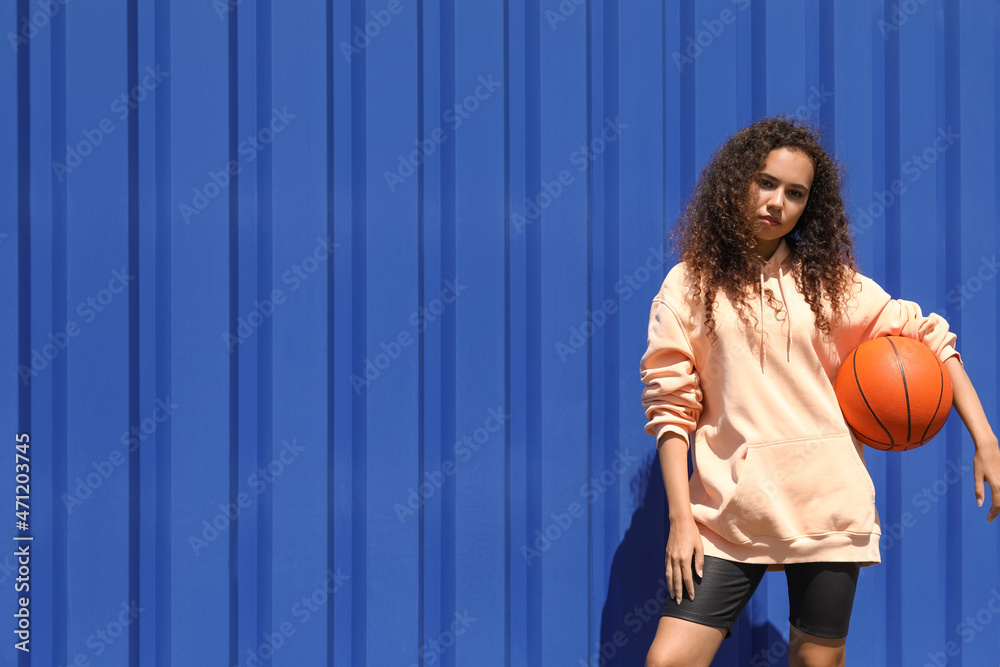Wall mural beautiful young african-american woman in stylish hoodie and with ball outdoors - Wall murals
