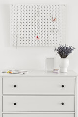 White chest of drawers with lavender bouquet and peg board on light wall background