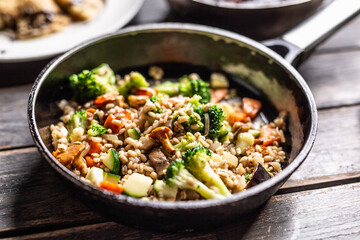 Healthy vegan meal of groats served with broccoli, carrots, and mushrooms in a pan