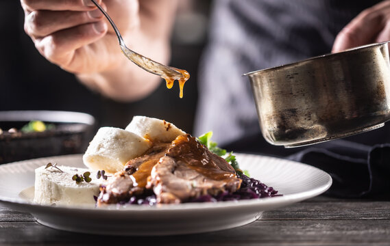 Detail of chef's hand pouring sauce over pork slice with dumplings and red cabbage