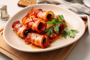 Plate with delicious prunes baked in crispy bacon, gravy and parsley on wooden board, closeup