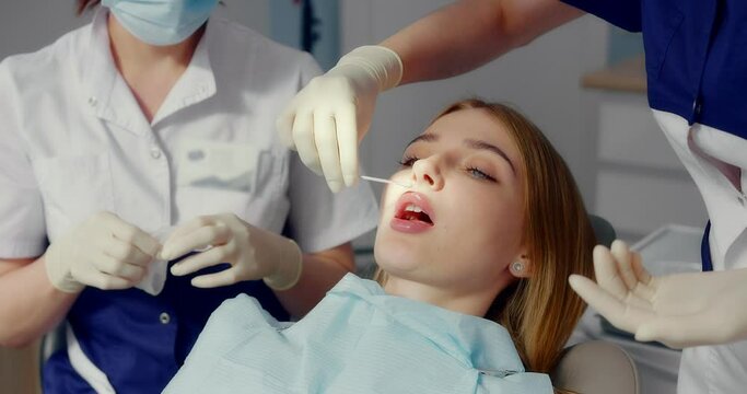 The assistant prepares the patient before applying the retractor. A dentist applies a retractor to a female patient before professional teeth cleaning in a modern dental office. Shot with RED