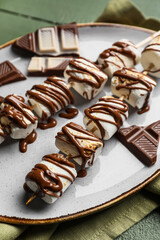 Plate of tasty grilled marshmallows on green wooden background
