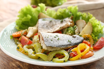 Plate of tasty sea bass fish with vegetables on wooden background, closeup