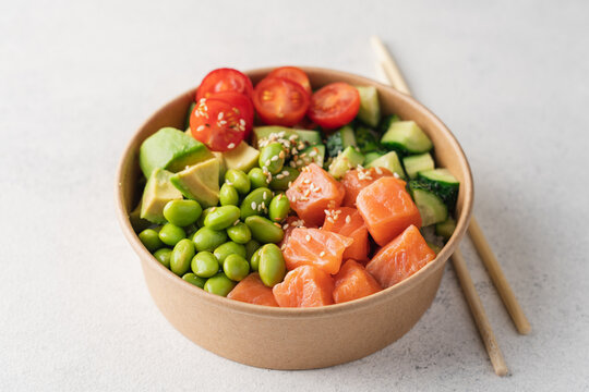 Salmon, avocado, cucumber, tomato, edamame beans and rice poke bowl on light gray background