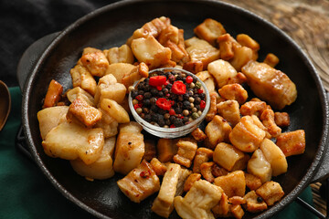 Frying pan with tasty cracklings on wooden background