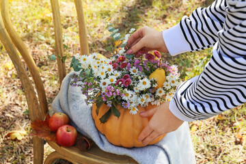 Woman making beautiful bouquet of autumn flowers in pumpkin outdoors