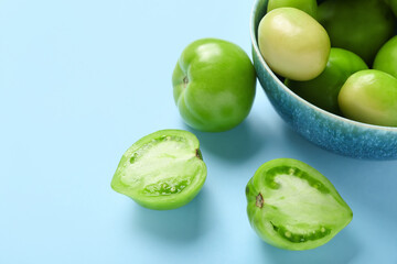 Bowl with fresh green tomatoes on blue background, closeup