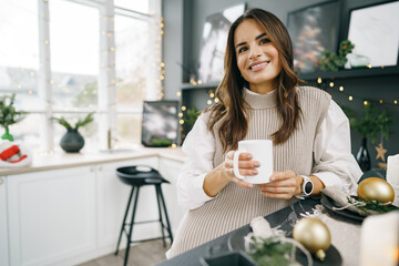 Attractive young woman drinks tea in the kitchen for Christmas