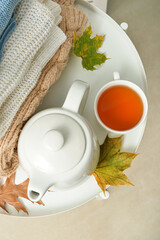 Tea pot, cup of hot beverage and autumn leaves on table in room