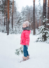 Fototapeta na wymiar Little girl in a bright jacket plays in the winter forest