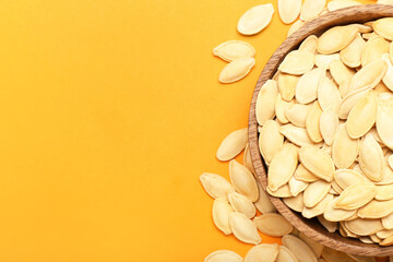 Bowl with natural pumpkin seeds on orange background, closeup