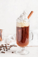 Glass cup of tasty coffee with cinnamon on light background