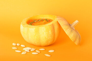 Tasty cream soup served in pumpkin and seeds on color background