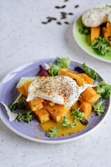 Baked pumpkin slices with poached egg on a green plate over grey table. Seasonal autumn food vegetarian recipe.