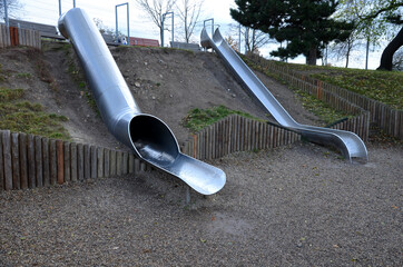 stainless steel slide on the field with grassy hills and wooden palisades. Large glossy tube for...