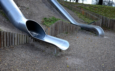 stainless steel slide on the field with grassy hills and wooden palisades. Large glossy tube for...