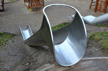 stainless steel slide on the field with grassy hills and wooden palisades. Large glossy tube for sliding children with an impact on the tartan rubber pad. the end of the tube is an open trough