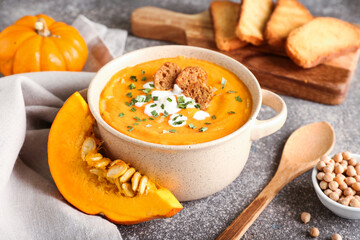 Pot with delicious pumpkin cream soup on grey background
