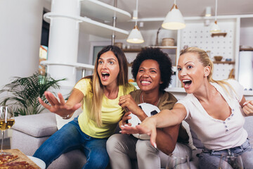 Group of female friends sitting at home cheering, watching a football game.