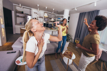 Naklejka premium Young woman singing in to microphone at home party having fun. Bachelorette party, karaoke, music concert and holidays concept