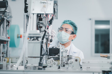 Both male and female Asian scientists are outfitted with protective gear. Examining the factory's machinery and materials used in the mask-making process. Covid 19 is a piece of preventive equipment.