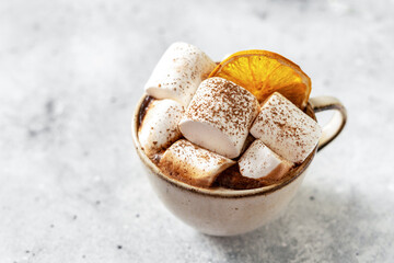 Traditional Christmas cocoa in a ceramic cup with marshmallows and orange chips on a light background