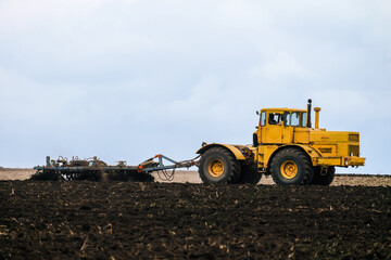 Big powerful wheeled yellow tractor pulls the disc harrow plowing the field