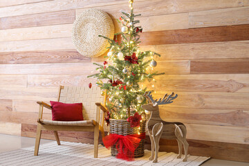 Christmas tree with glowing lights, armchair and reindeer near wooden wall