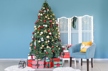 Beautiful Christmas tree, gift boxes and armchair near blue wall