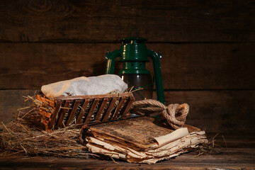 Manger with baby, old book and lantern on wooden background. Concept of Christmas story