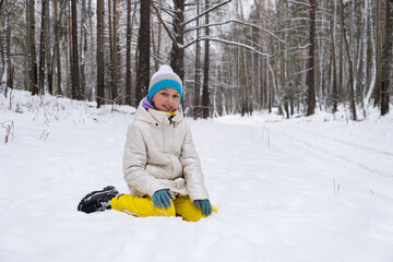 a girl is sitting in the snow in the forest