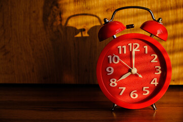 Red alarm clock early morning on table, shadows from blinds background.