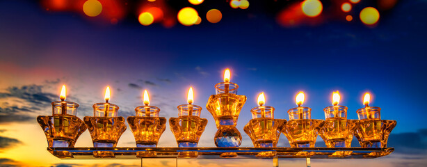 Crystal festive menorah and burning candles with olive oil as symbol of Hanukkah - Jewish Holiday of Miracle Light. Blurred background of mountains and dramatic sky, digitally generated festive bokeh 