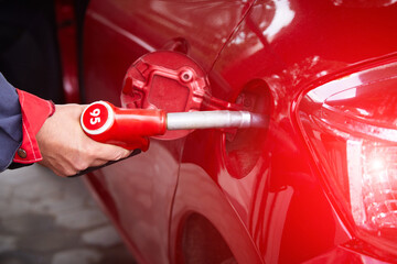 A man fills up a car's tank with gasoline at an equipped gas station. A hand holds a refueling gun in the tank of the car, close-up.