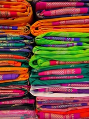 Closeup view of stacked colours saris or sarees in display of Indian retail shop, textile shop.