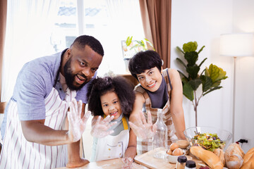 Happy African American family enjoy together while prepare the flour for making cookies at home. Look at camera.