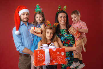 Merry Christmas and happy holidays. Dad, mom and kids exchange gifts on red background. Parents and children standing and smiling holding gift boxes in their hands. loving family with gifts in studio.