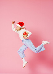 happy smiling girl with gift boxes with red ribbons in her hands and a Santa hat on her head jumps on a pink background. Preparation for Christmas, discount sale. Dynamic image.